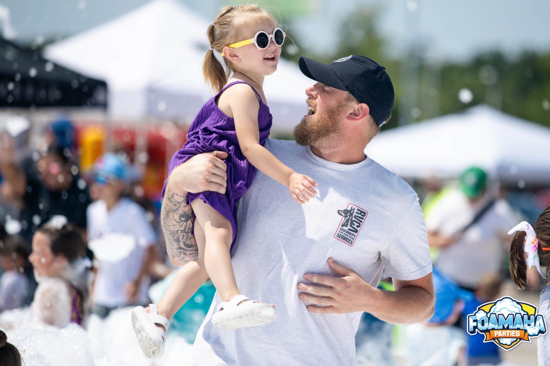 Dad lifting his daughter in sunglasses up in the air at a foam event