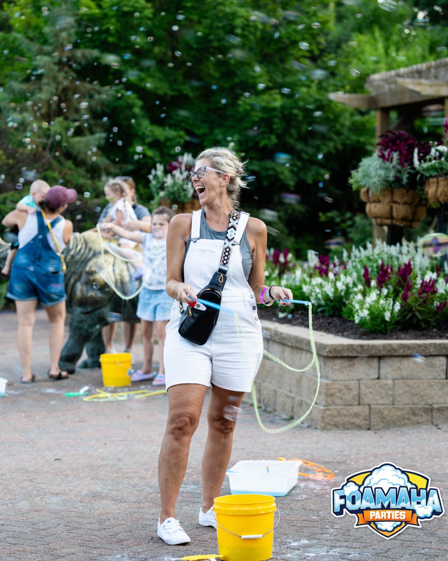 Woman in white overalls laughing while making giant bubbles in a garden